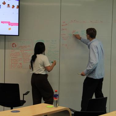 Two people are collaborating and writing on a whiteboard in a meeting room.