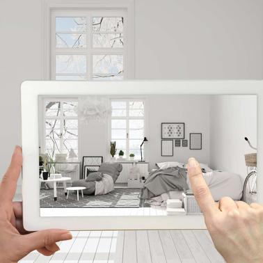 Hands holding a tablet displaying a virtual interior design of a modern living room within a minimalist styled room.
