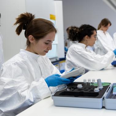 A group of scientists wearing lab coats and gloves are working in a laboratory setting.