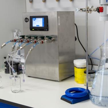 A laboratory setup featuring a device with multiple tubes connected to glass containers and a flask filled with liquid.