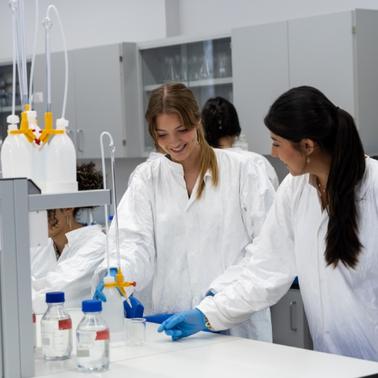 Two young women are collaborating in a laboratory setting, working with lab equipment.
