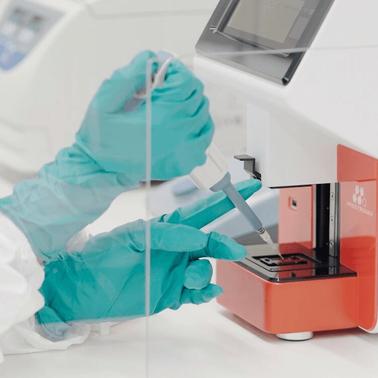 A person in protective gloves is using a laboratory device for testing.
