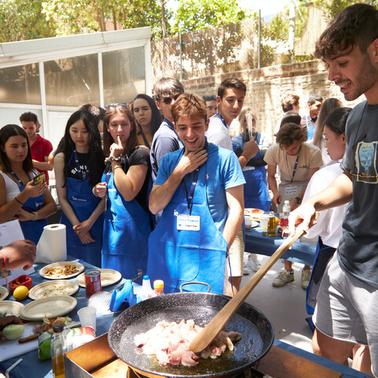A lively outdoor cooking class with diverse participants engaging in food preparation.