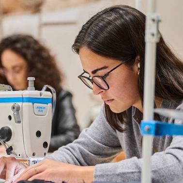 A woman is sewing fabric with a sewing machine in a workshop setting.