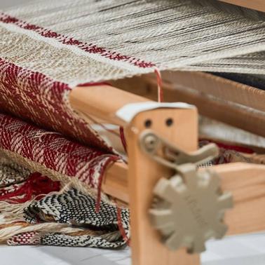 A wooden loom displaying various intricately patterned textiles.