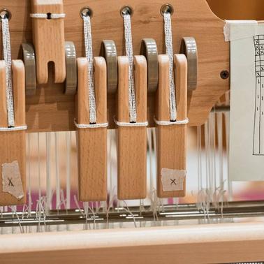 A close-up view of a loom showing wooden levers and tensioned threads.