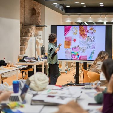 A person is presenting colorful design samples on a screen to an audience in a creative workspace.