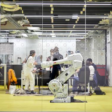 A group of people collaborating in a modern workspace with a robotic arm in the foreground.