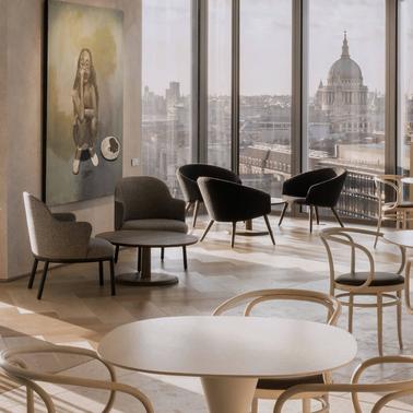 A modern office lounge with stylish furniture and large windows overlooking a cityscape.