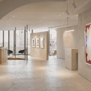 A modern art gallery interior with abstract paintings displayed on white walls, under a curved ceiling with natural light coming through large windows.