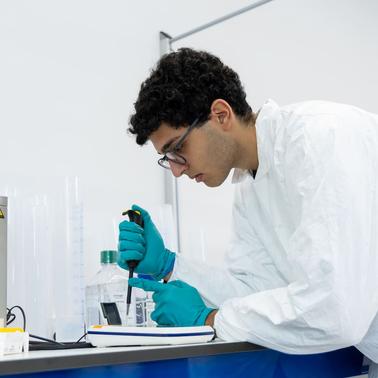 A researcher in a lab coat is using a micropipette to measure liquid in a laboratory setting.