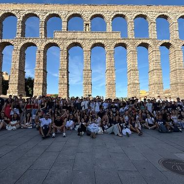 A large group of people gathered in front of a historic aqueduct under a clear blue sky.