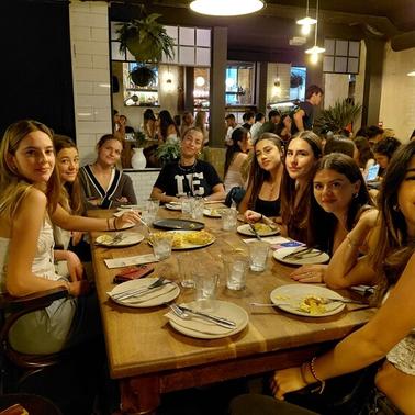 A group of eight young women sitting around a dining table in a lively restaurant.