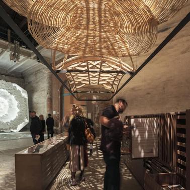 An art installation featuring intricate woven structures suspended from the ceiling in an industrial space.