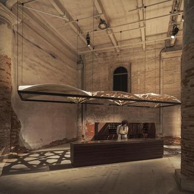 An artistic installation featuring a suspended structure above a wooden counter in an industrial space.
