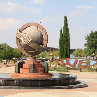 A large globe with the Warner Bros logo is located in a park setting.