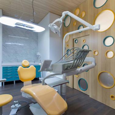 A modern dental office with a stylish interior design featuring a yellow dental chair and decorative circular mirrors on the wall.