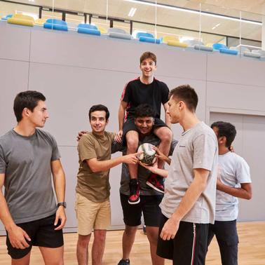 A group of young men engaging in a casual game of indoor soccer, celebrating together in a sports hall.