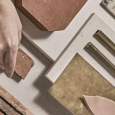 A hand arranging various material samples like ceramic, metal, and concrete on a table.