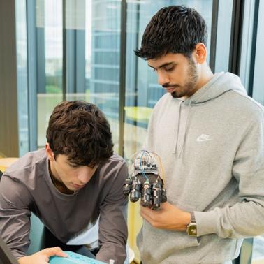 Two young men are collaborating on a robotics project in a modern office environment.