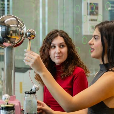 Two women are engaged in a science experiment involving a Tesla coil.