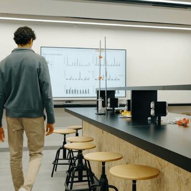 A person walking away in a modern laboratory with a large display showing graphs.