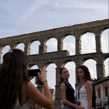 Three young women are posing for a photo in front of an ancient aqueduct in a lively setting.