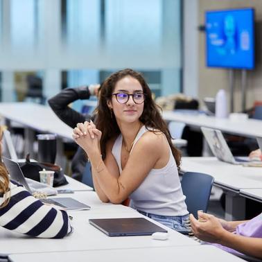 A group of students engaged in a discussion around a table in a classroom setting.