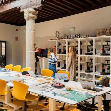 A modern workspace featuring tables, chairs, and multiple 3D printers in a well-lit room.