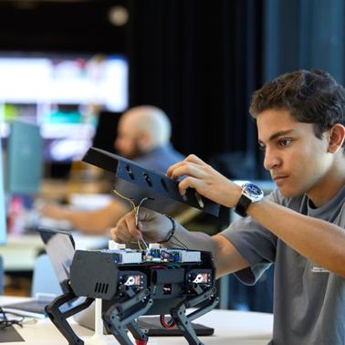A young man is assembling a robotic device at a workstation.
