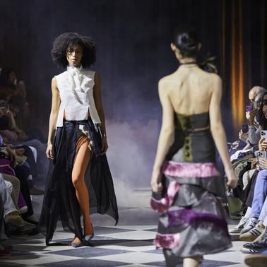 Models showcase fashion designs on a runway surrounded by an engaged audience.