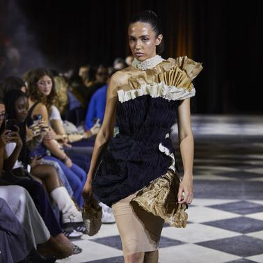 A model walks down the runway wearing a unique and artistic dress during a fashion show.