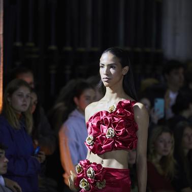 A model showcases a stunning red outfit adorned with floral details while a captivated audience looks on.