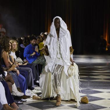 A model walks down the runway wearing an elegant white outfit at a fashion show.