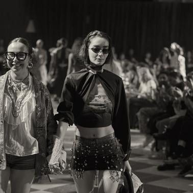 Two models walk hand in hand on the runway during a fashion show.