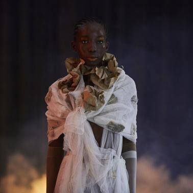 A model stands confidently in a creatively styled outfit surrounded by mist.