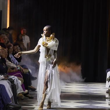 A model walks down the runway wearing an elegant outfit surrounded by an audience.