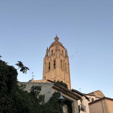 A tall bell tower rises against a clear blue sky with birds flying around it.