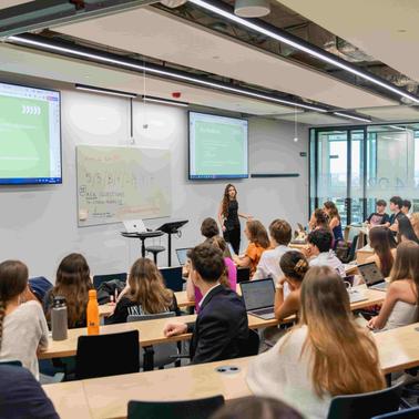 A person is presenting in a classroom full of students seated at desks with laptops.