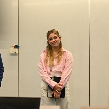 A woman stands smiling in a presentation room next to a man in formal attire.