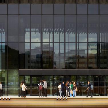 A group of people is gathered outside a modern glass building.