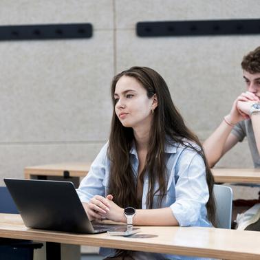 A student is listening attentively while another student appears to be thinking in a classroom setting.