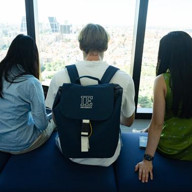 Three people are sitting together, looking out over a cityscape through large windows.