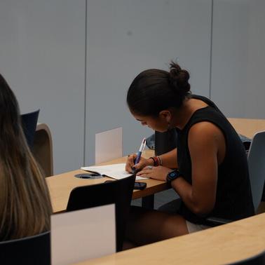 A student is writing notes at a desk in a classroom setting.