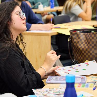 A student is focused on her work while surrounded by classmates in a classroom setting.