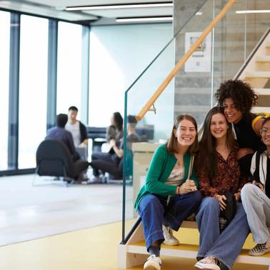 Four young adults smiling and sitting on yellow stairs in a modern indoor setting.