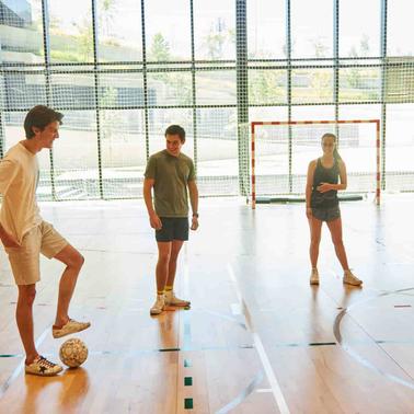 Four young adults are standing in an indoor sports court, preparing to play soccer.