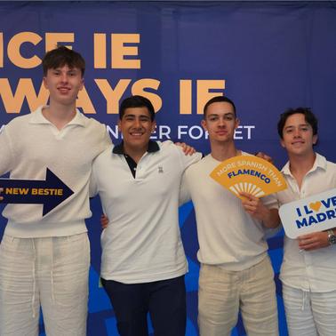 A group of four young men posing together with cheerful expressions and signs at an event.