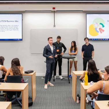 A group of students presents a business idea in a modern classroom while others listen.