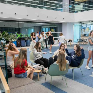 Groups of young people chatting and relaxing in a modern office lobby with large windows.